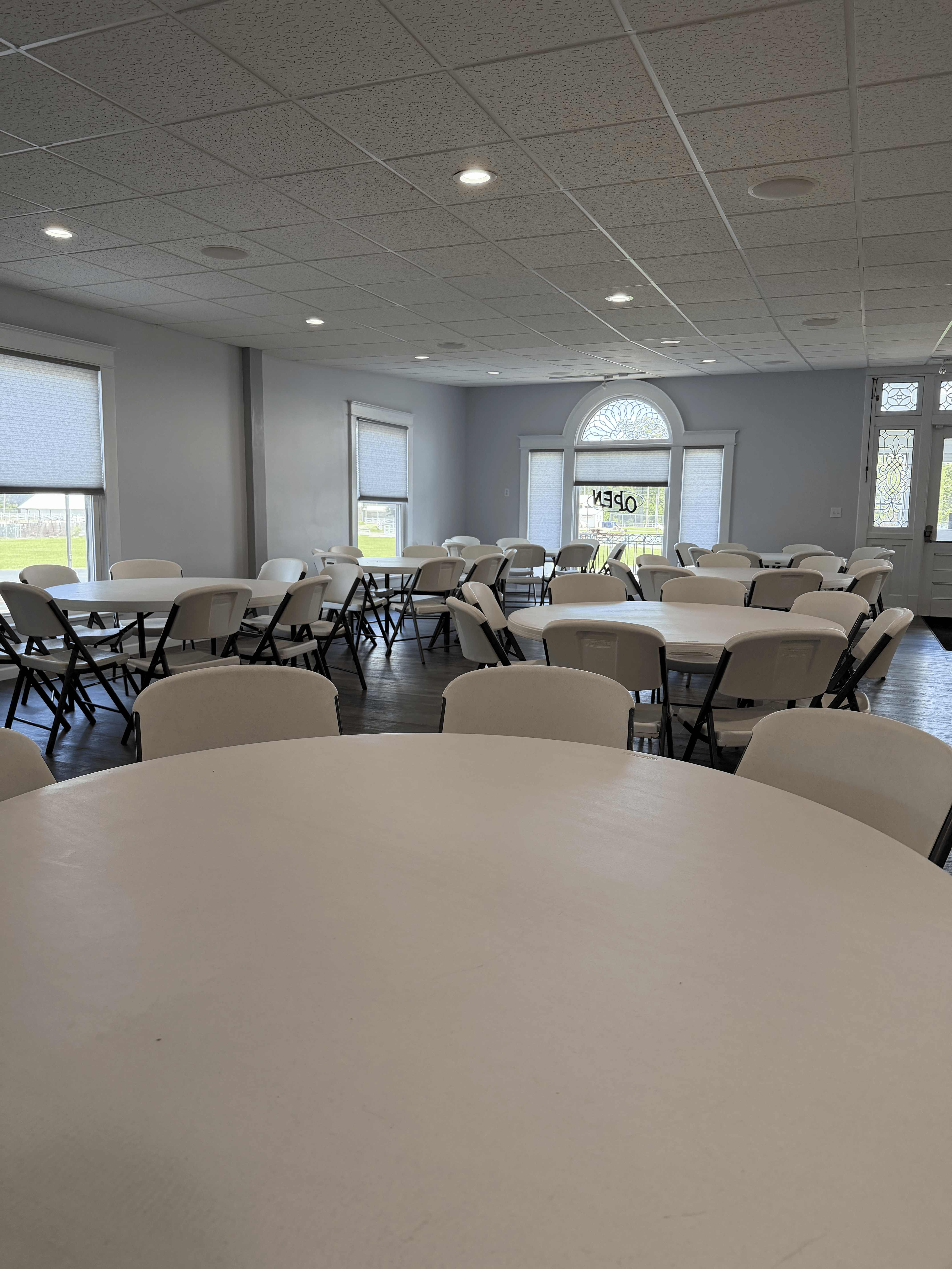 Round banquet tables with white folding chairs and natural light from arched windows